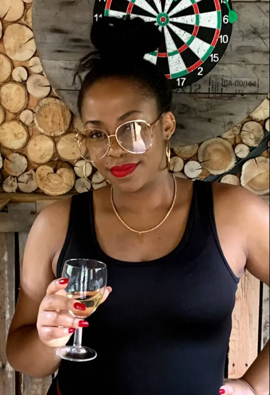 MissKalunji smiling in gold glasses and holding a glass